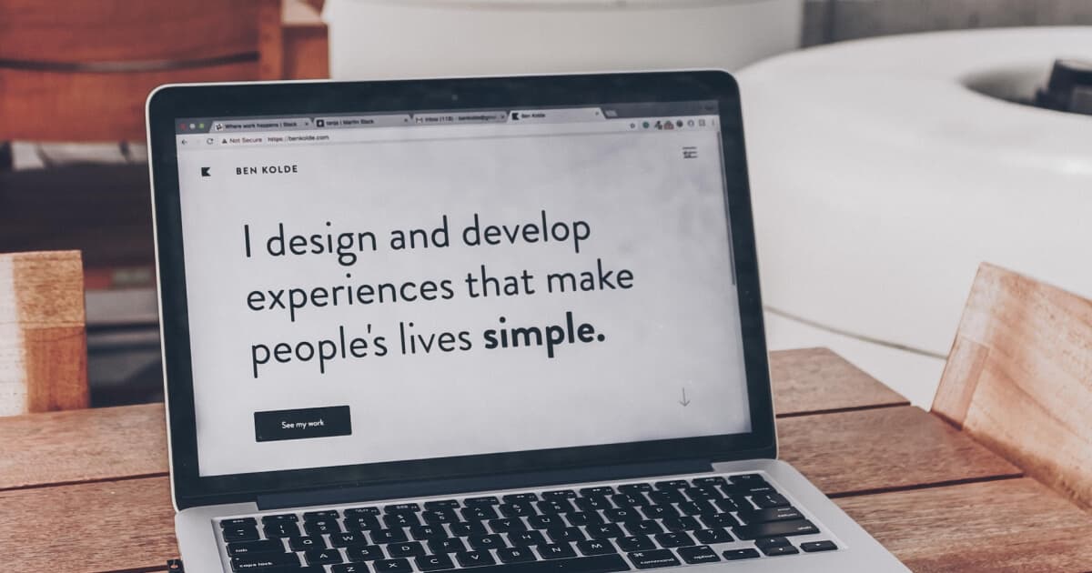 laptop z wyświetloną sentencją "I design and develop experiences that make people's lives simple" leży na stole